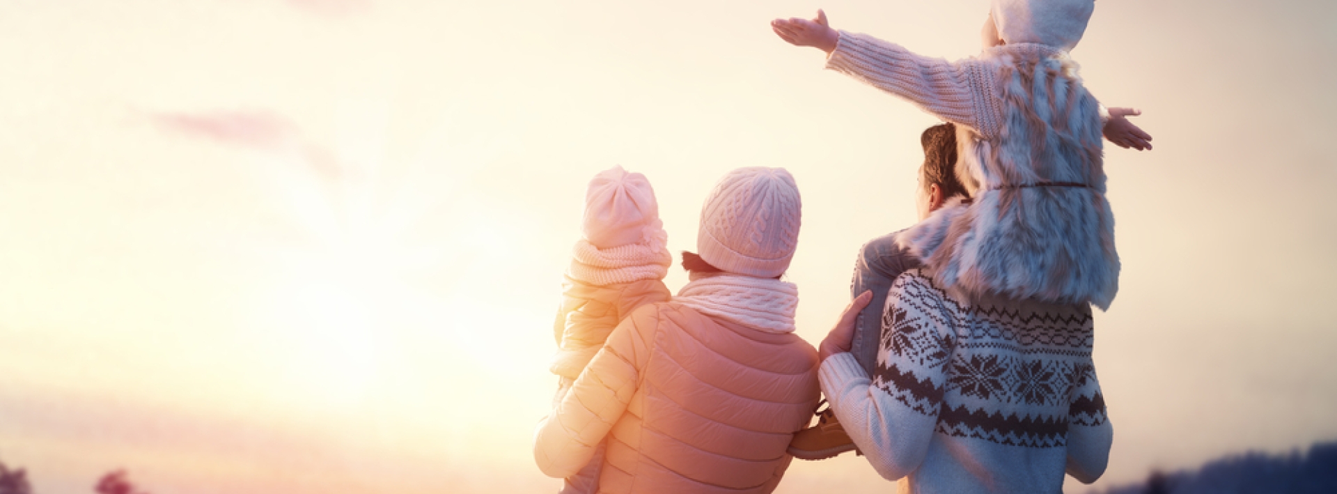 Couple holding two kids, one in fathers should spreading her arms as the sun hits them all.